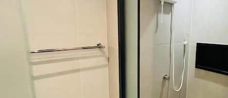 A modern bathroom with a glass shower enclosure, a towel rack, and a wall-mounted control panel.