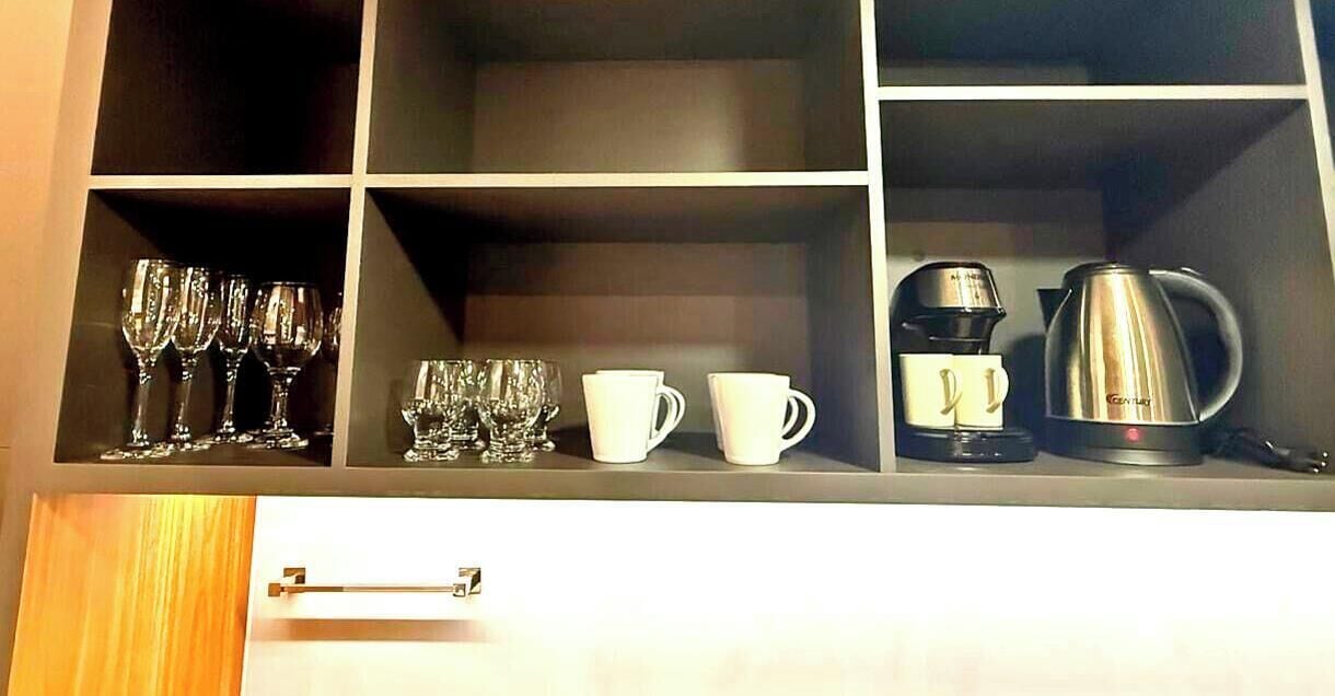 A kitchen cabinet with wine glasses, cups, and a coffee maker.