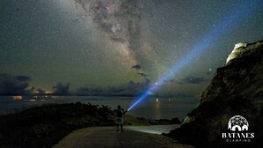A person standing on a beach under a starry sky with a visible Milky Way and a beam of light. - Batanes Glamping (Sabtang)