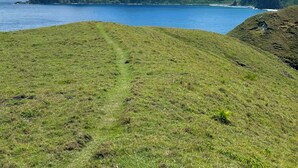 A grassy landscape with a clear view of a mountain range and a body of water. - Batanes Glamping (Sabtang)