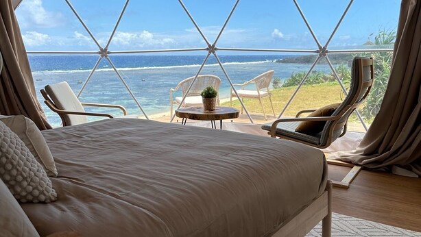 A tented room with a bed, two chairs, a small table, and a view of the ocean. - Batanes Glamping (Sabtang)