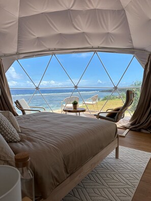 A tented room with a bed, two chairs, a small table, and a view of the ocean. - Batanes Glamping (Sabtang)