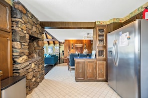 A kitchen with a stone accent wall, wooden cabinets, a stainless steel refrigerator, and a dining area with blue chairs.