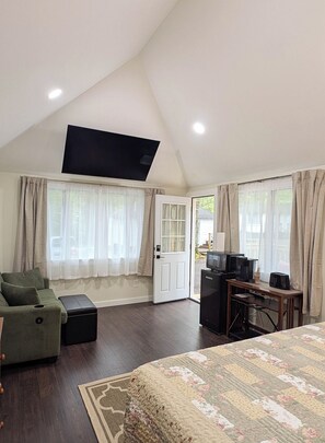 A spacious room with a large bed, a sofa, a television mounted on the ceiling, a coffee machine, and a desk.