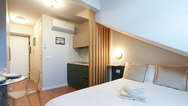 A hotel room with a bed, a small kitchenette, a dining area with a table and chairs, and a bathroom.