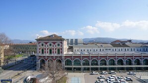 A large building with a central tower and multiple arched windows, surrounded by a parking lot and a clear sky.