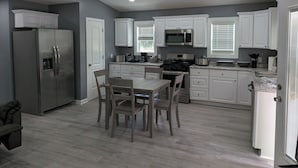 Een moderne keuken met witte kastjes, roestvrijstalen apparatuur en een eethoek met houten stoelen.