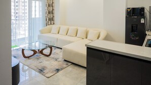 A modern living room with a glass coffee table, a beige sofa, a kitchen area with a refrigerator, and a large window with curtains. - Welcome to Summerville homes ,the cozy haven nestled in the heart of Nairobi. (Nairobi)