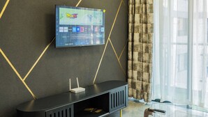 A modern living room with a flat-screen TV mounted on a wall, a glass-top coffee table, and a black entertainment unit with a router. - Welcome to Summerville homes ,the cozy haven nestled in the heart of Nairobi. (Nairobi)