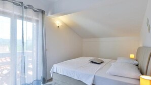 Une chambre à coucher avec un lit, une lampe de chevet et une fenêtre ornée de rideaux légers.
