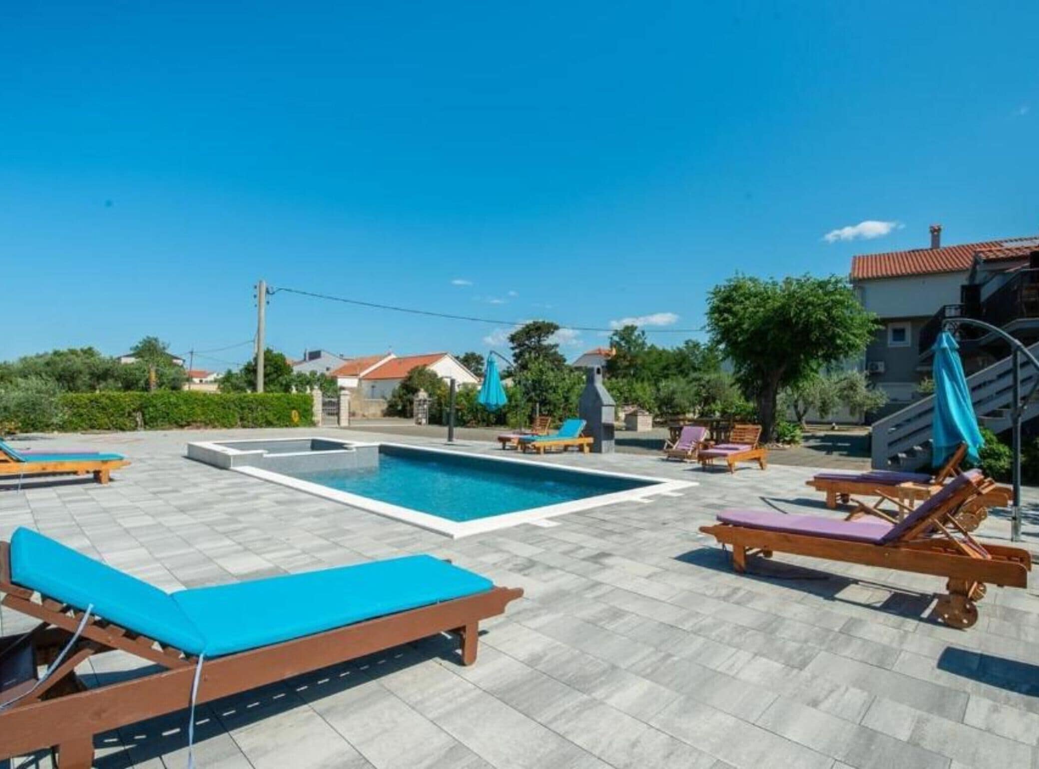Un espace piscine doté de nombreuses chaises longues et d’une terrasse carrelée en pierre.
