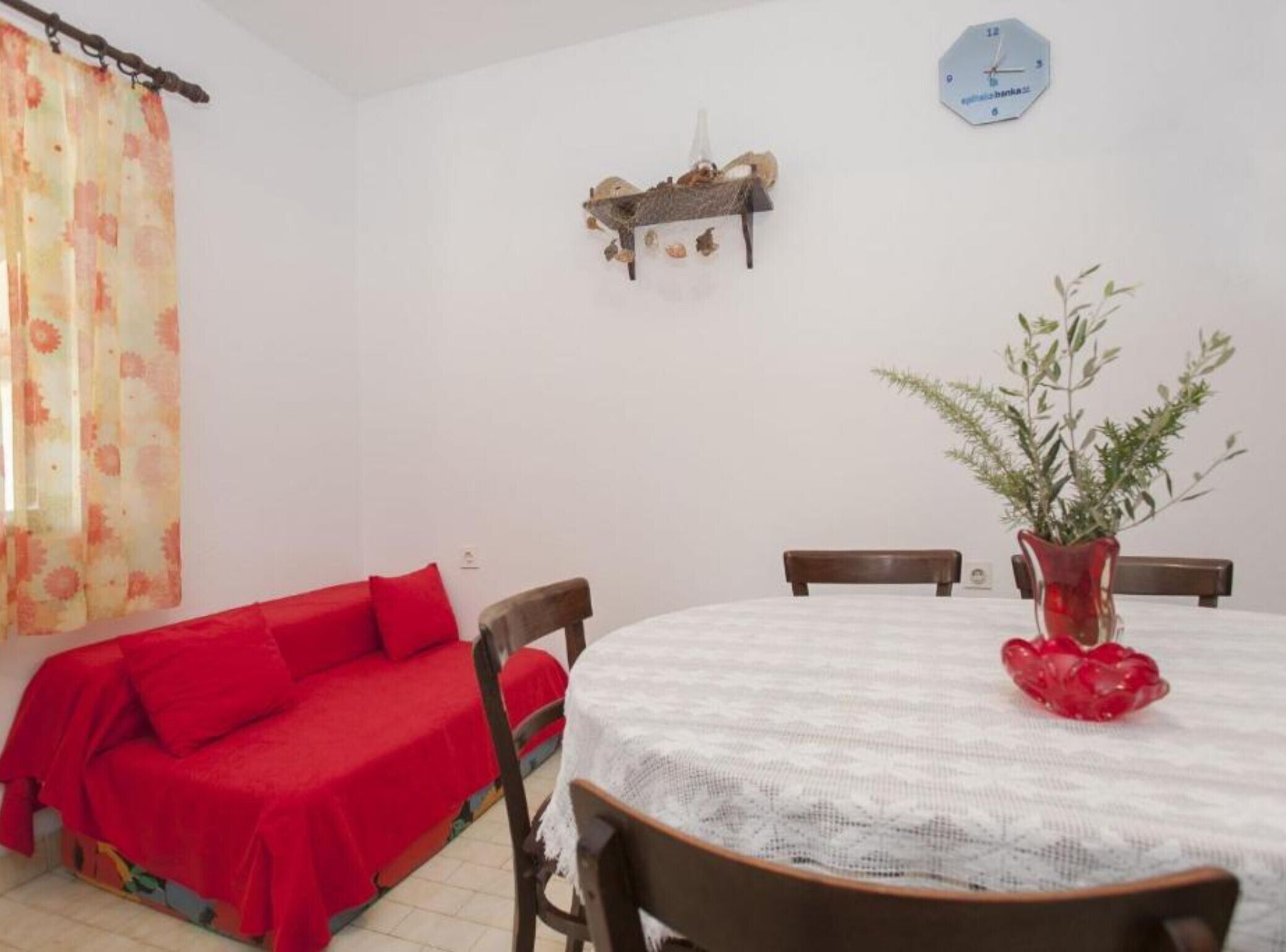 A dining area with a round table, red sofa, and a clock on the wall.