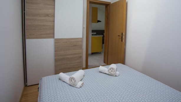 A bedroom with a bed, two rolled towels, a wardrobe, and a door leading to another room.