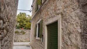 A narrow stone alleyway with a building featuring a green shuttered door and a window with shutters.