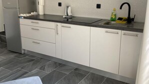 Una cocina moderna con armarios blancos, un refrigerador de acero inoxidable, una encimera negra, un fregadero y una tetera.