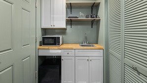 Une cuisine de taille réduite avec des meubles blancs, un four à micro-ondes, un évier et un plan de travail en bois.