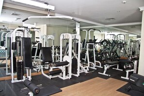 Uma academia com diversos equipamentos de exercício, espelhos e piso de madeira.