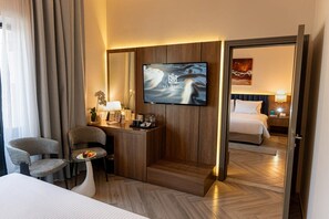 A hotel room with a bed, a desk with a flat-screen TV, a chair, a small table with a fruit bowl, and a mirror. - Majestic Central Hotel (Dubai)