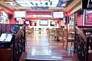 Un bar deportivo con varias pantallas, sillas y mesas de madera.