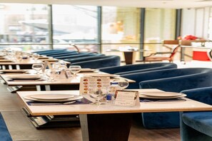 En restaurang med bord som är dukade för middag, blå klädda sittplatser och ett menyställ.