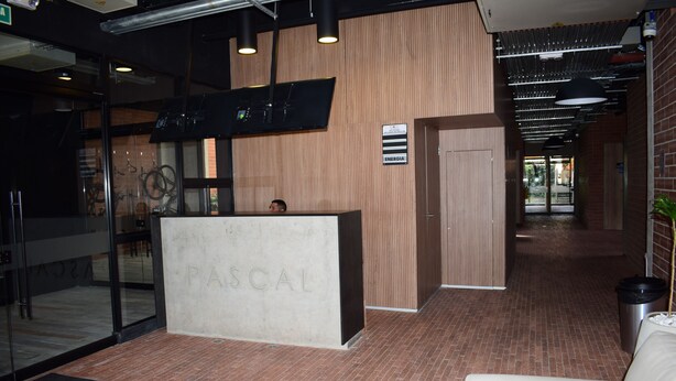 A reception area with a reception desk labeled 'PASCAL', a glass door entrance, and a brick floor.
