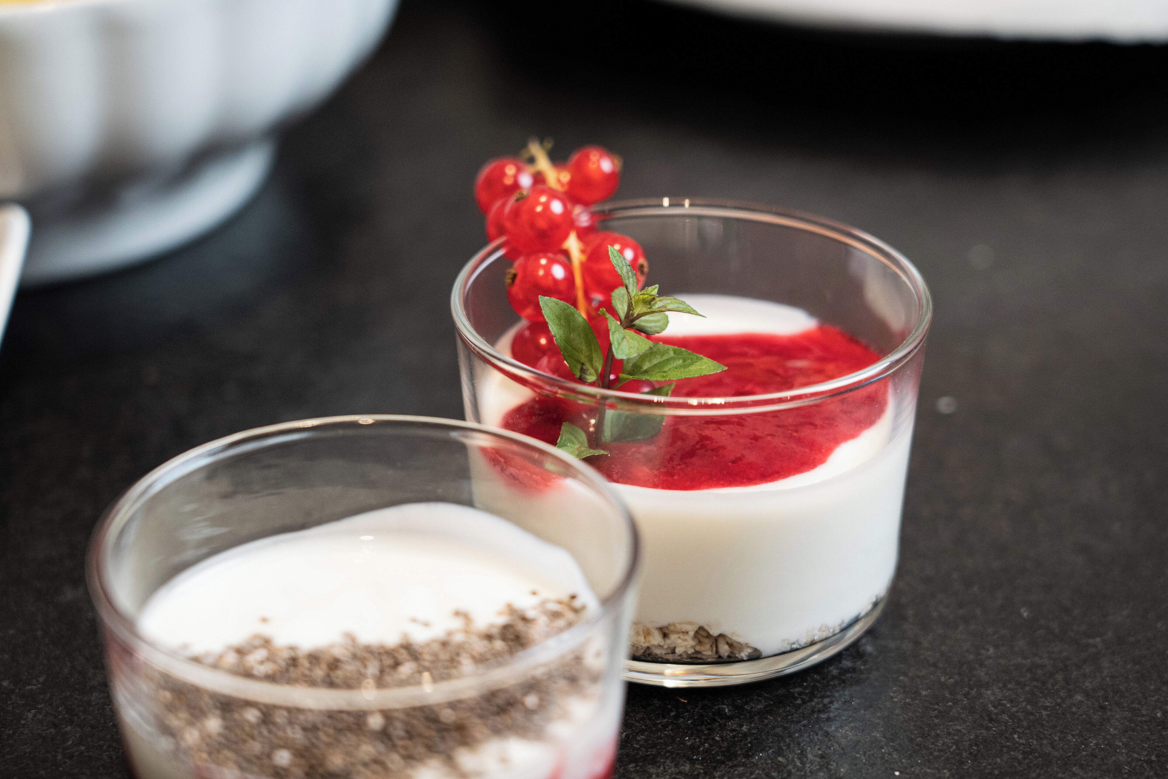 Dos vasos con postre, frutos rojos y una hoja de menta, sobre una superficie oscura.
