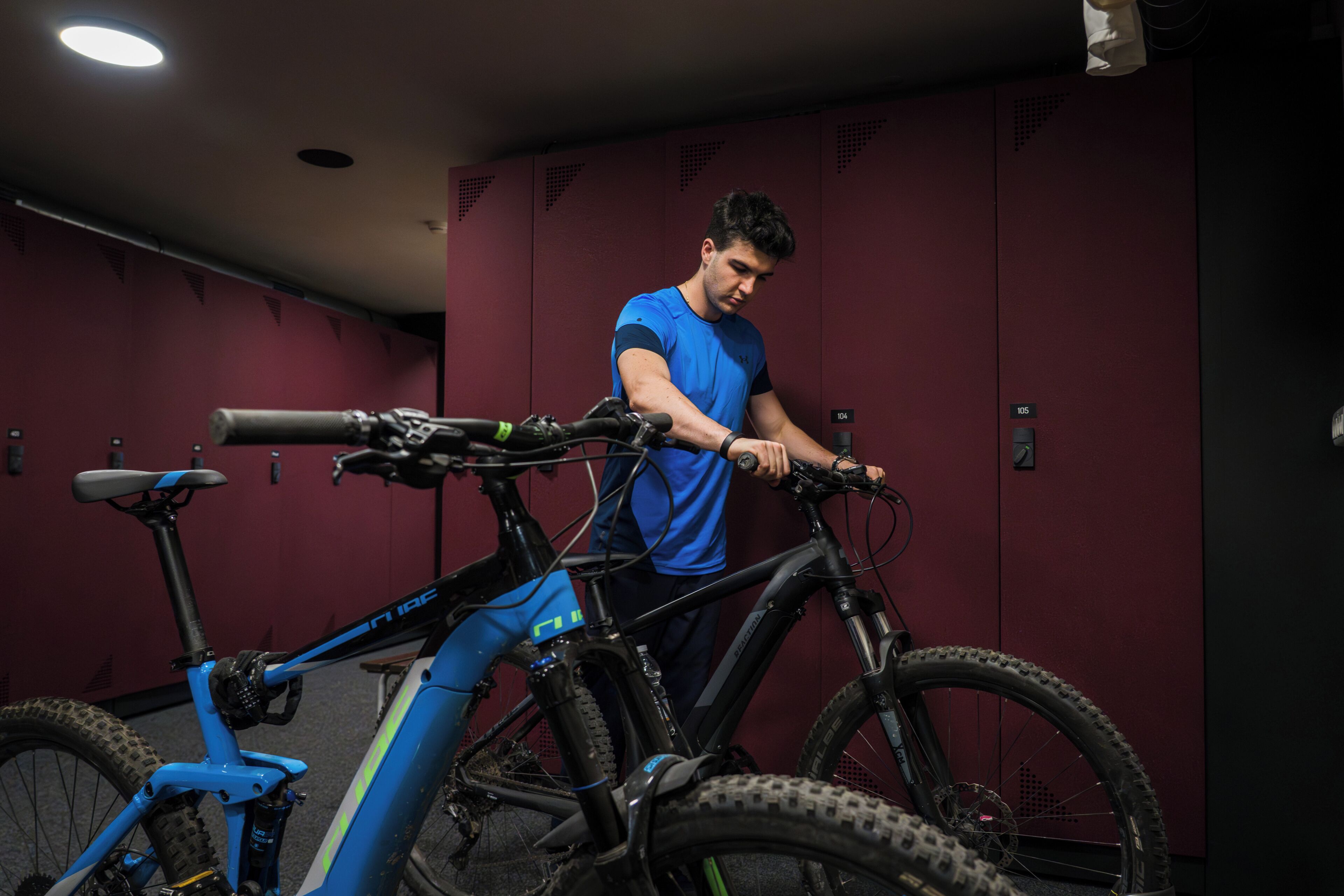 Una persona ajustando una bicicleta en una habitación con taquones rojos y una lámpara en el techo.