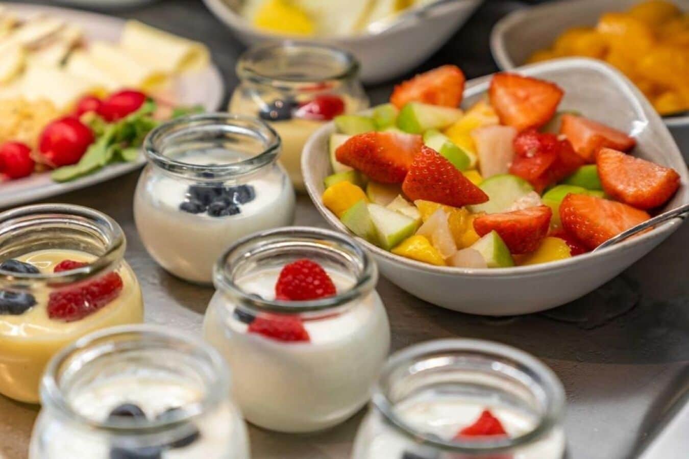 A variety of food items including yogurt with berries, a bowl of mixed fruits, and other dishes.