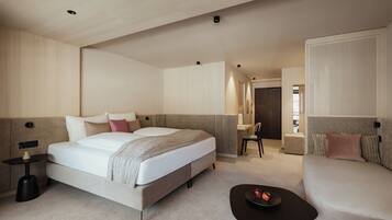 A modern hotel room with a large bed, a sofa, a small table with fruit, and a desk with a chair.