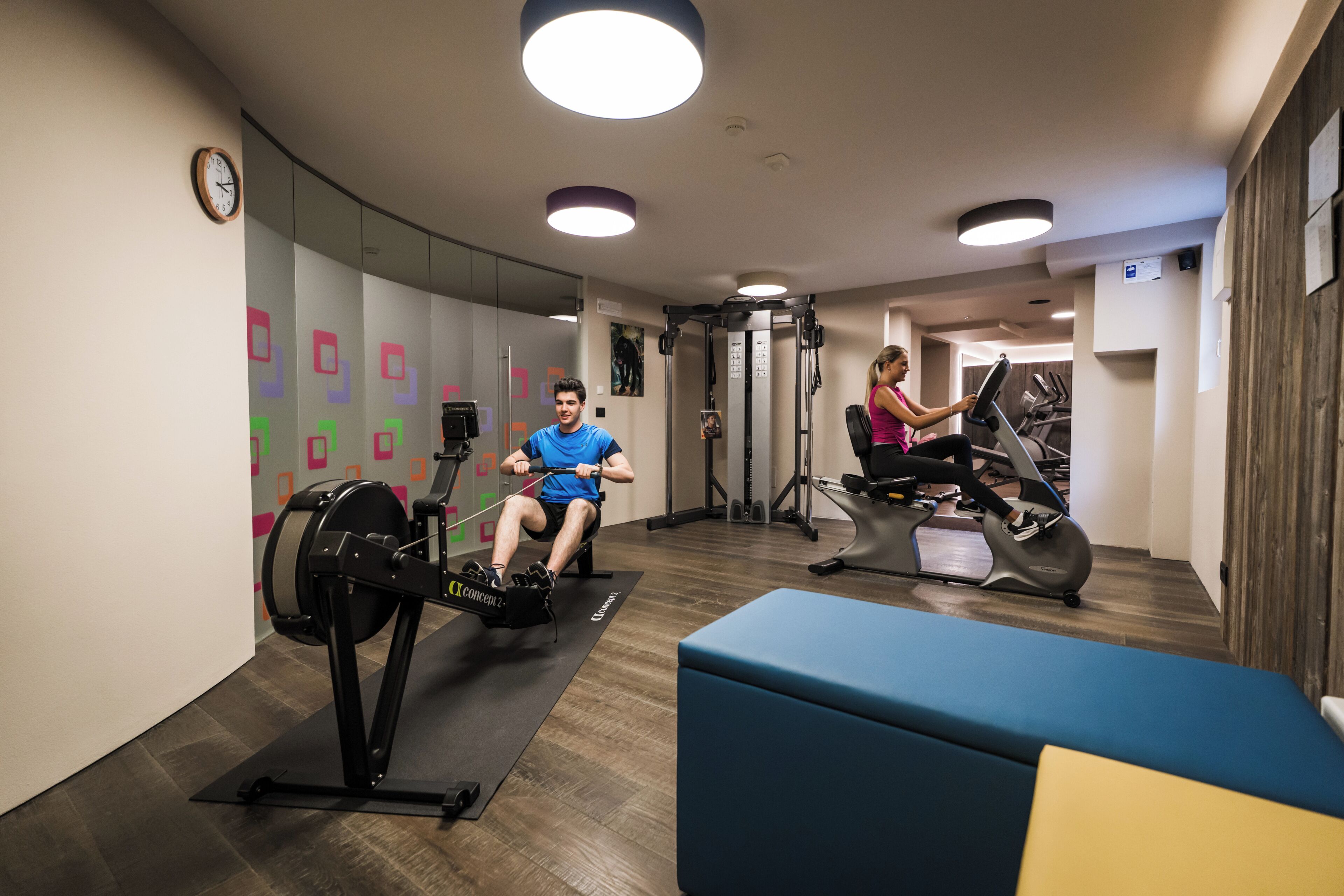 Un gimnasio con máquinas de cardio, una banca de pesas y un reloj de pared.