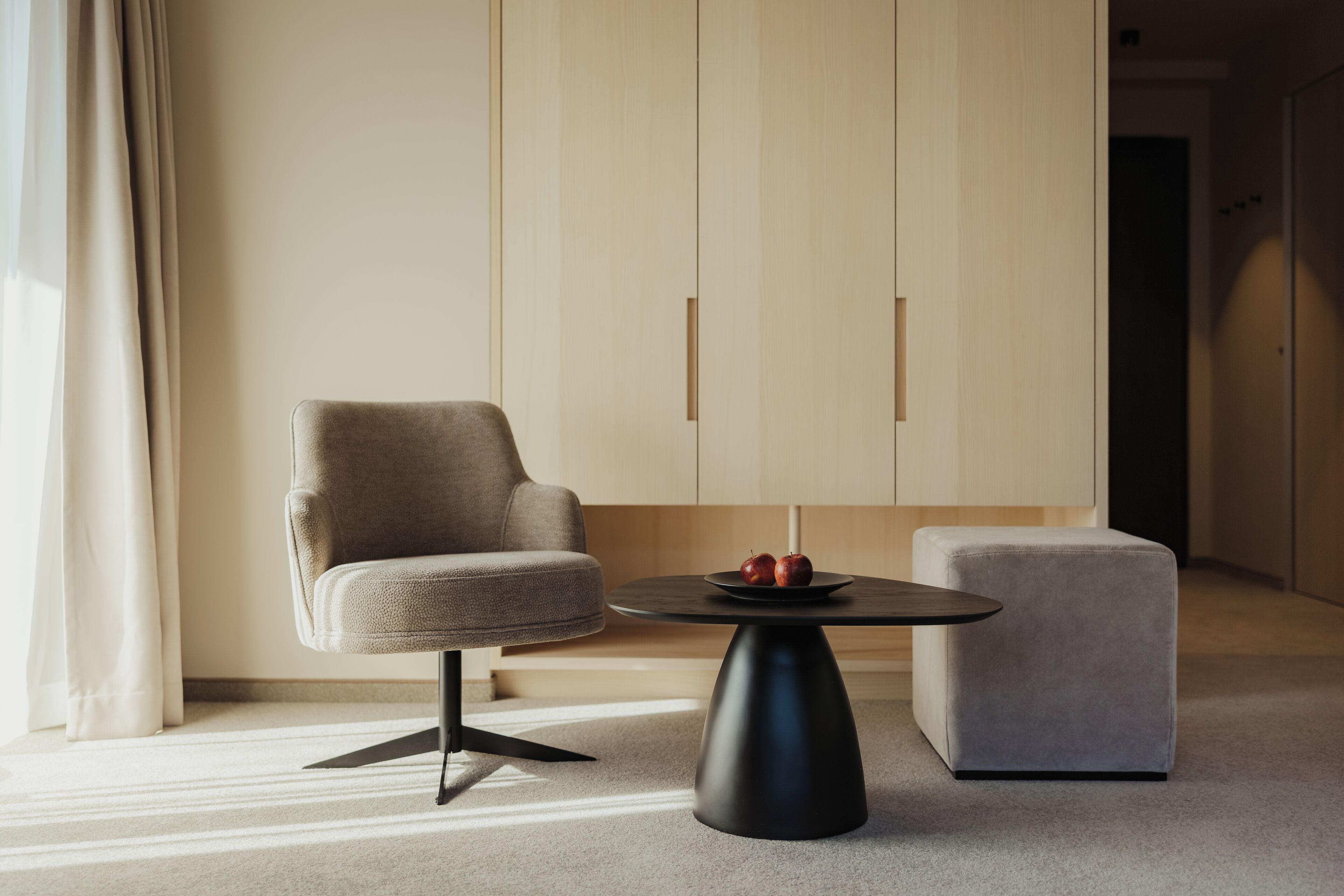 Una habitación moderna con un sillón gris, una mesita redonda con manzanas y un reposapiés gris.