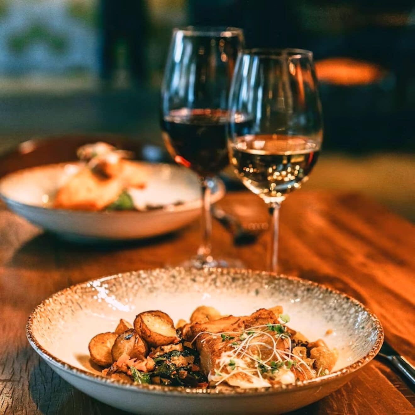 Una mesa de madera con un plato de comida y dos copas de vino.