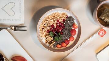 Een ontbijttafel met een kom yoghurt belegd met granola, bessen en zaden, een kopje thee, en een kaartje met een hartsymbool.