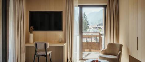 A modern hotel room with a desk, chair, and a balcony with a view of mountains.