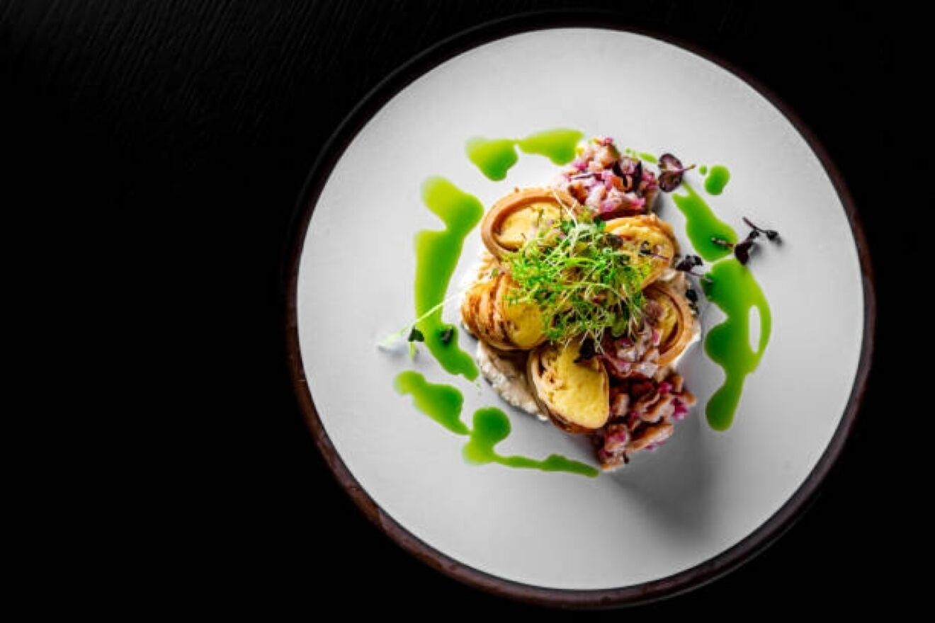 A white plate with a dish of food, garnished with green sauce and herbs.