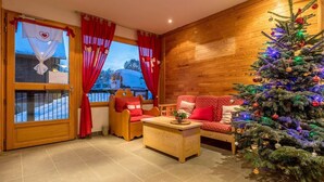 A cozy room with a wooden wall, a red sofa, a wooden coffee table, and a Christmas tree. - Wifi, 100m from ski slopes, swimming pool, sauna, terrace, balcony, parking, tv, ski locker, 56m² (Les Déserts)