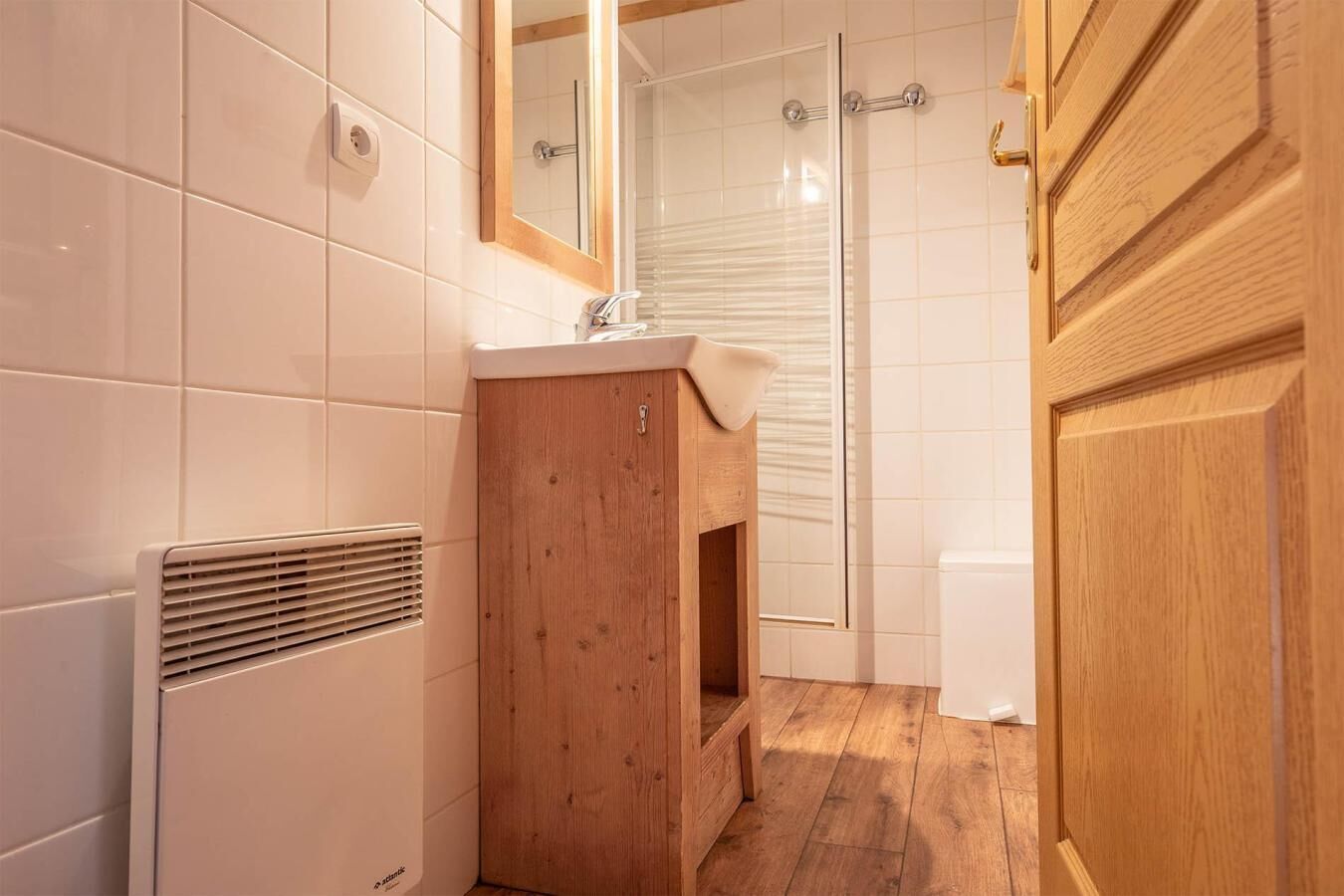 Une salle de bain avec des carreaux blancs, un meuble en bois, une douche avec une porte en verre et une porte en bois.