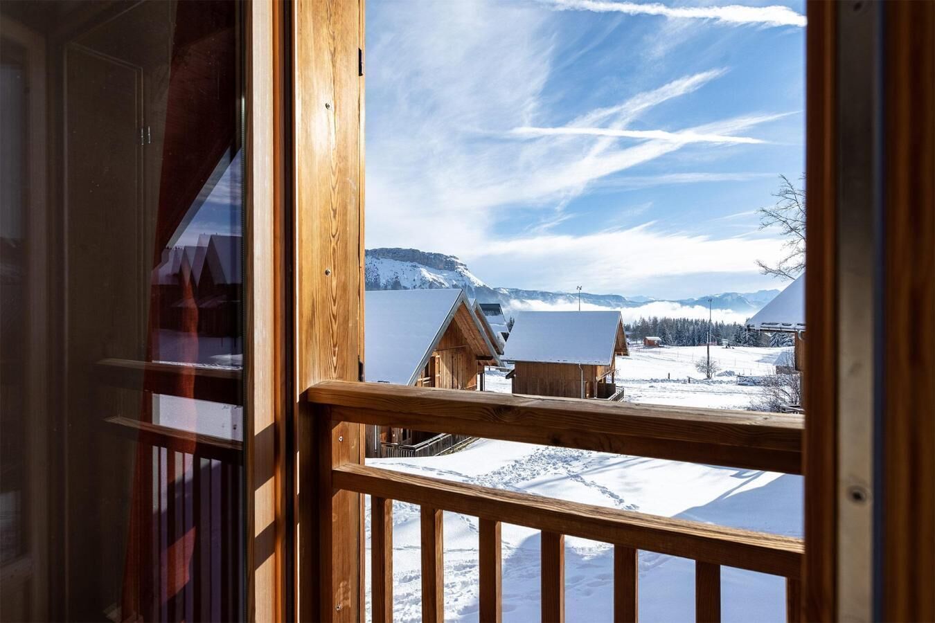 Un balcon en bois donnant sur un paysage enneigé, avec des montagnes en arrière-plan.