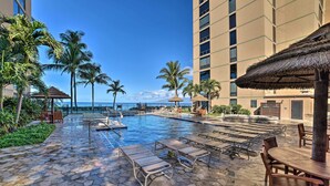 A pool area with lounge chairs, a stone pathway, and palm trees. - Island Views: Oceanfront Kaanapali Beach Penthouse (Lahaina)
