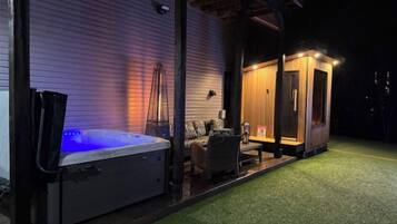 Een hottub buiten een gebouw, met een overdekte zithoek en een klein houten bouwwerk.