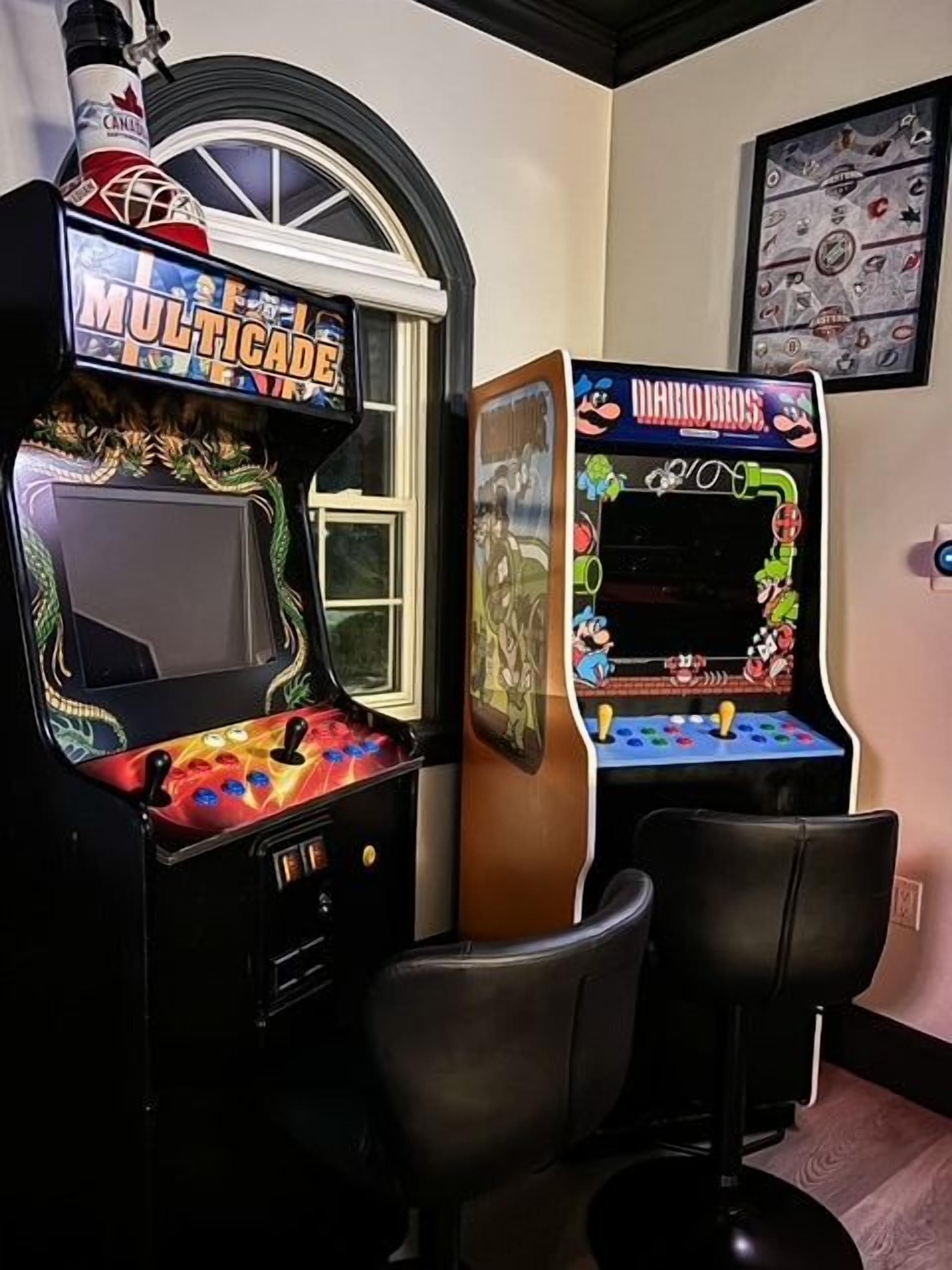 Two arcade machines, a window with a view, and a framed picture on the wall.