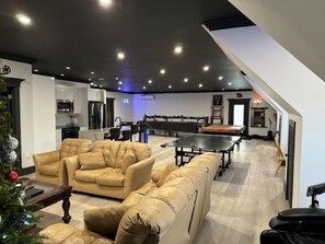 Amplia sala de estar con un sofá, mesa de ping pong y una cocina al fondo.