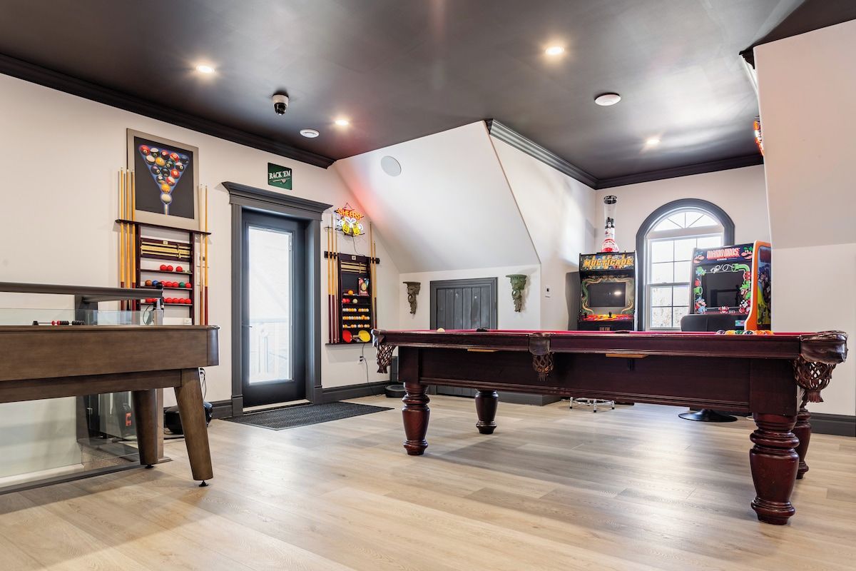 Una sala de billar con mesa de pool, portaobjetos para billar y dos máquinas de arcade.