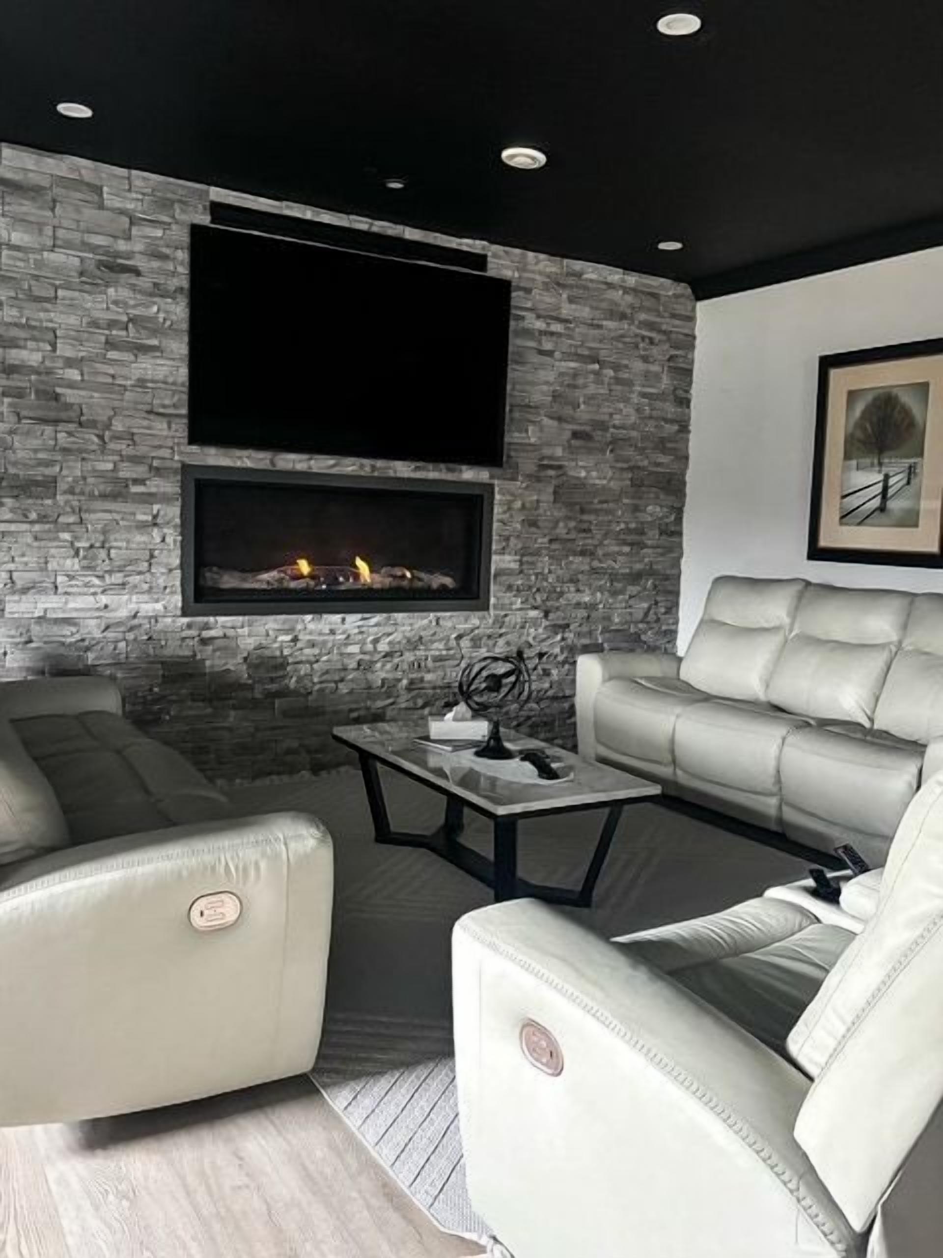 A modern living room with a fireplace, leather sofas, and a flat-screen TV mounted on a stone wall.