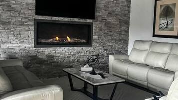 A modern living room with a fireplace, leather sofas, and a flat-screen TV mounted on a stone wall.