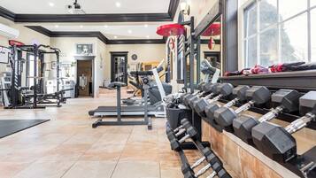 Een fitnessruimte met diverse trainingsapparaten, waaronder loopbanden, krachtapparaten en een dumbbellrek.