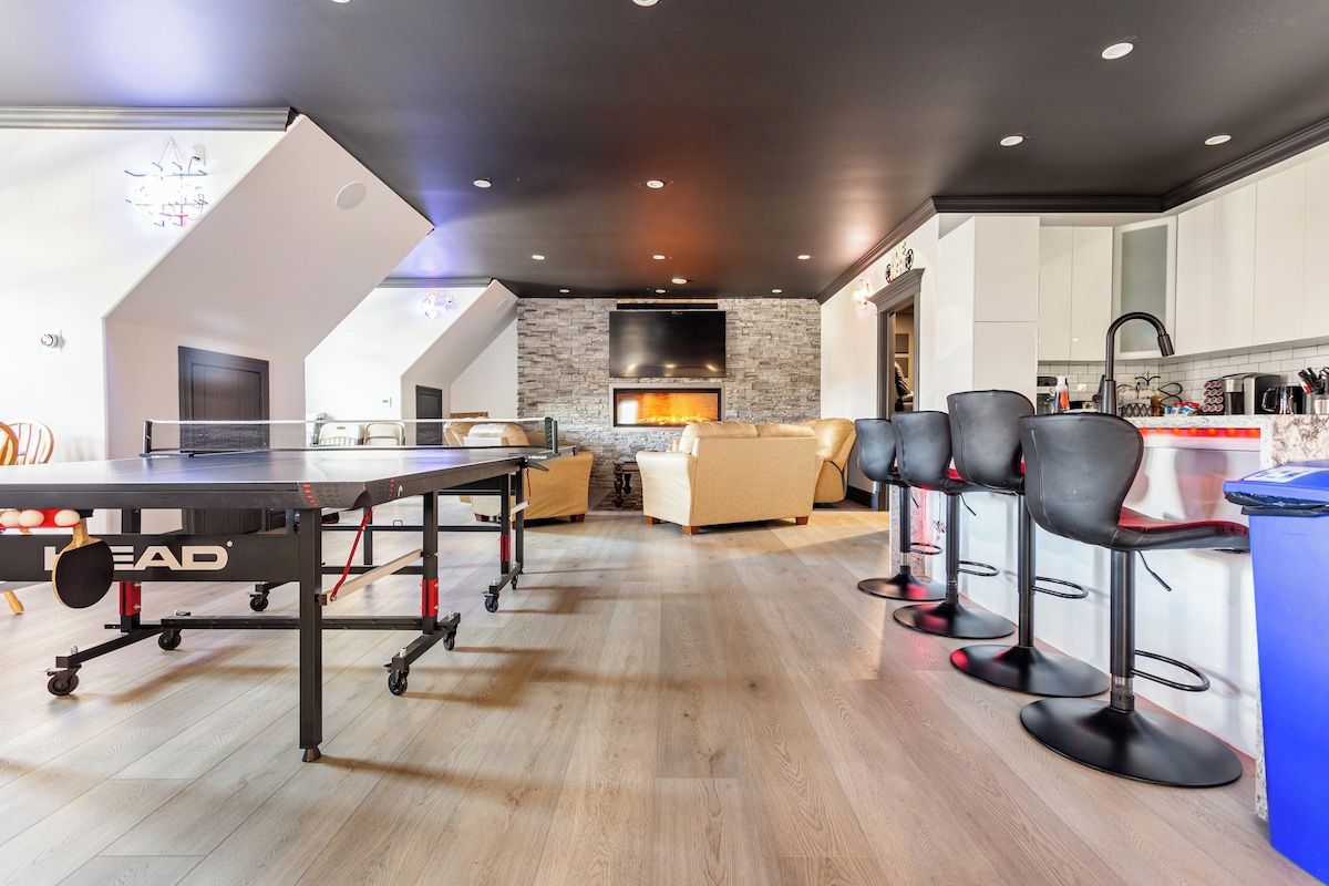 Un salon moderne avec une table de ping-pong, une cheminée et un coin cuisine doté de tabourets de bar.