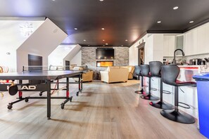 A modern living room with a ping pong table, a fireplace, and a kitchen area with bar stools.
