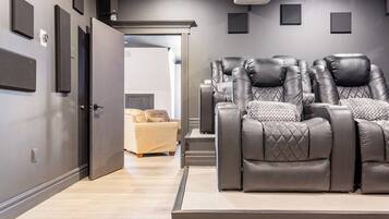 Una sala de cine en casa con un sofá de cuero reclinable, un sofá color beige y un proyector montado en el techo.