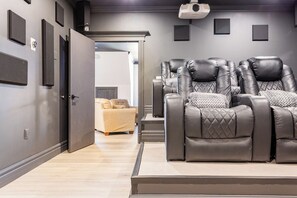 A home theater room with a reclining leather sofa, a beige sofa, and a projector mounted on the ceiling.